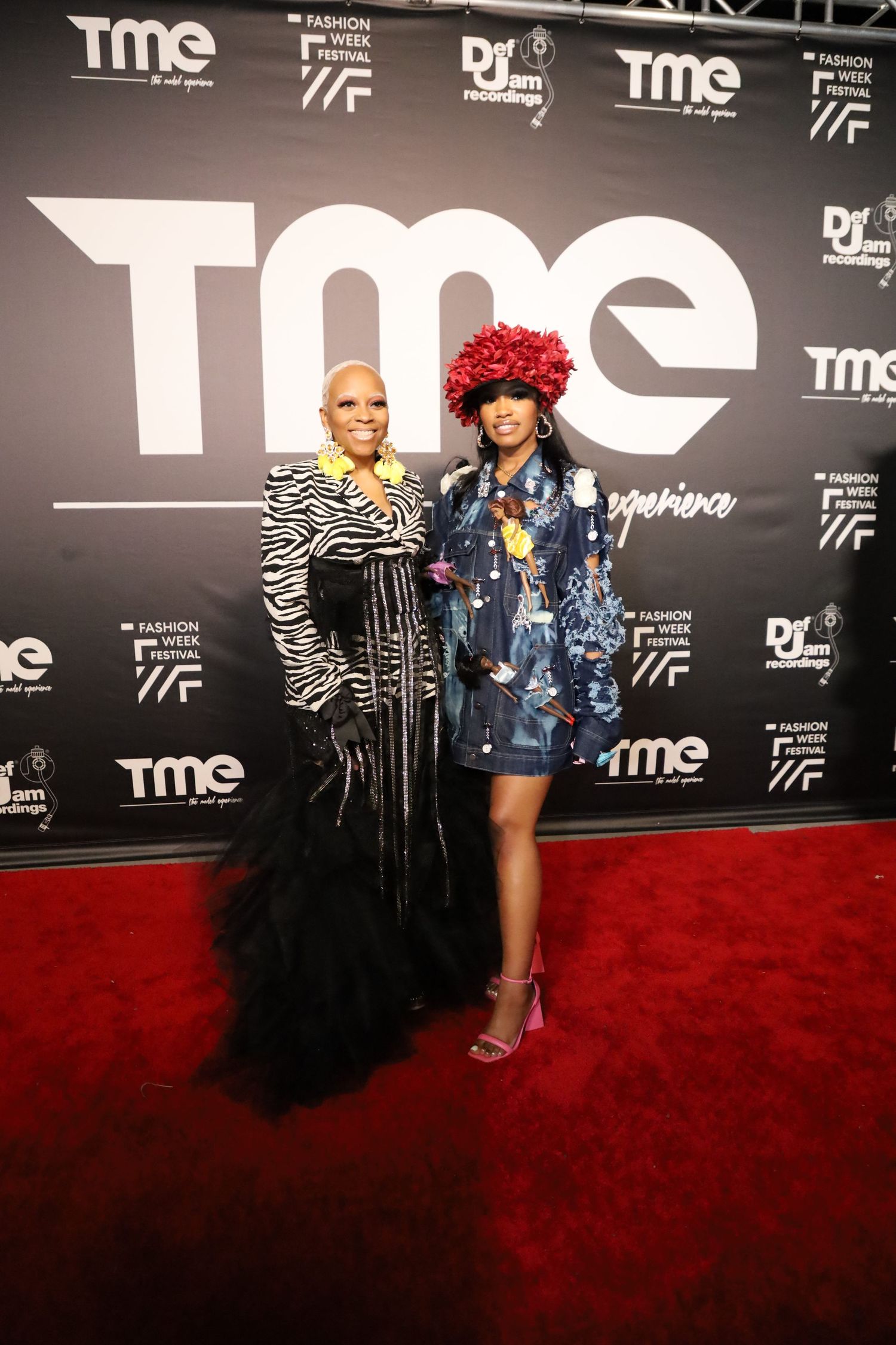 Event guests in bold outfits and colorful accessories pose against black TME branded backdrop.