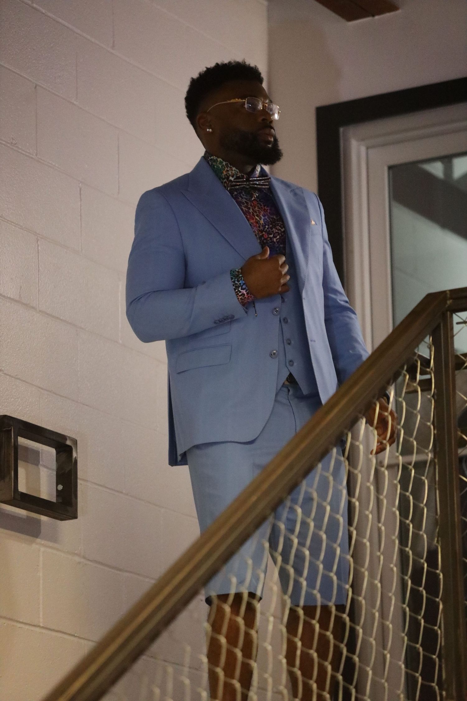 Individual in light blue suit jacket walking along railing in hallway.