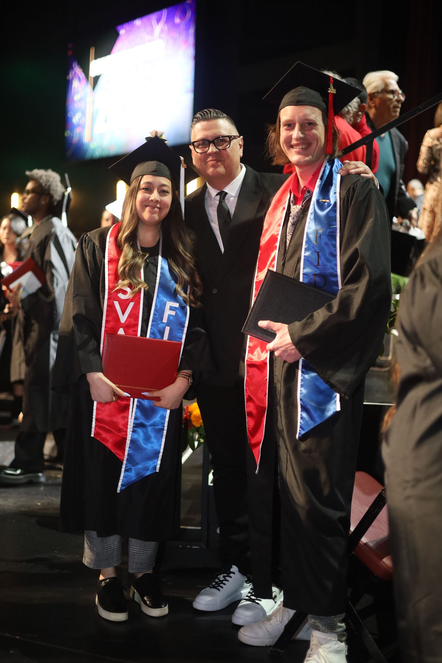 Graduates wearing colorful stoles and cords stand together during commencement.