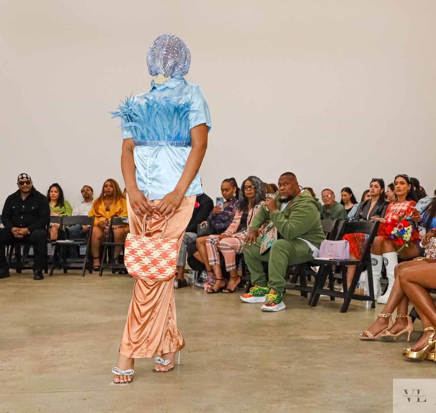 Model walks runway in blue top and peach checkered skirt at gallery event.
