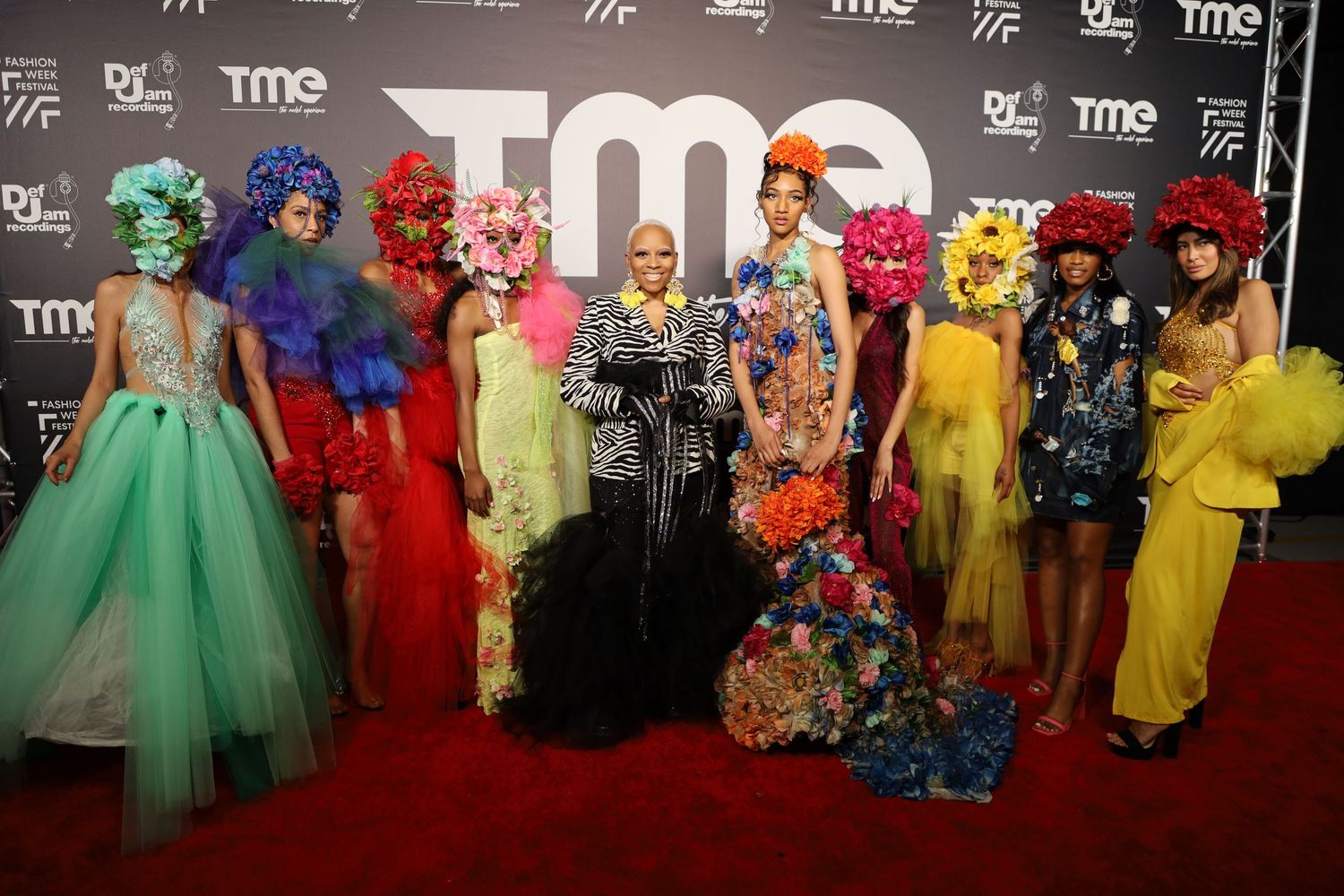 Group photo at fashion event showing diverse formal outfits including tulle gowns and bright ensembles.