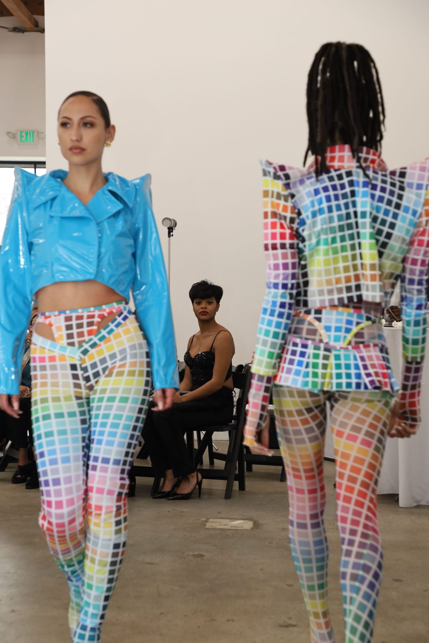 Models showcase vibrant rainbow grid-patterned catsuits with cropped jackets on the runway.