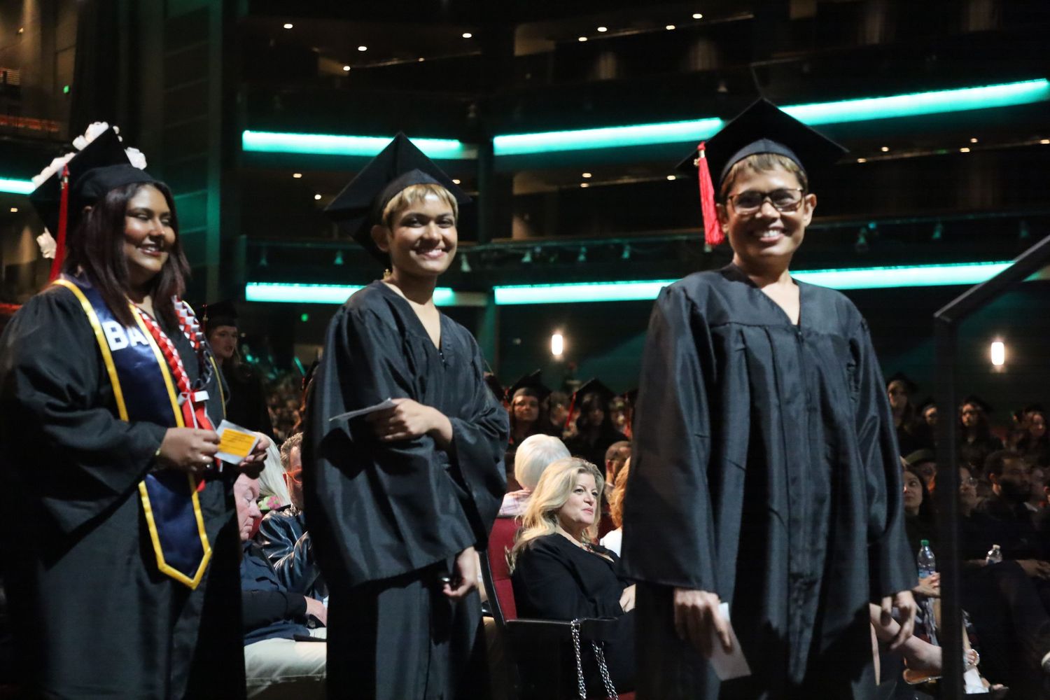 Three graduates smile while standing together in their black caps and gowns.