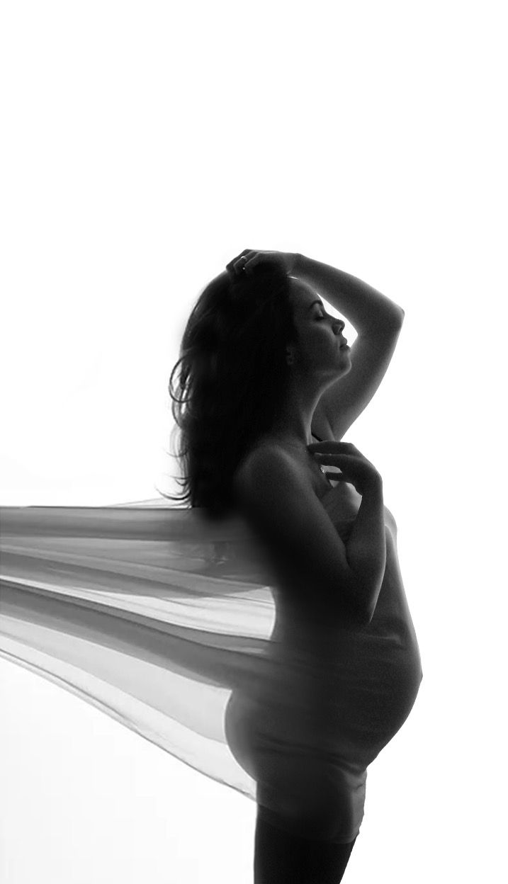 Black and white artistic silhouette photograph of a figure draped in flowing fabric against light background.
