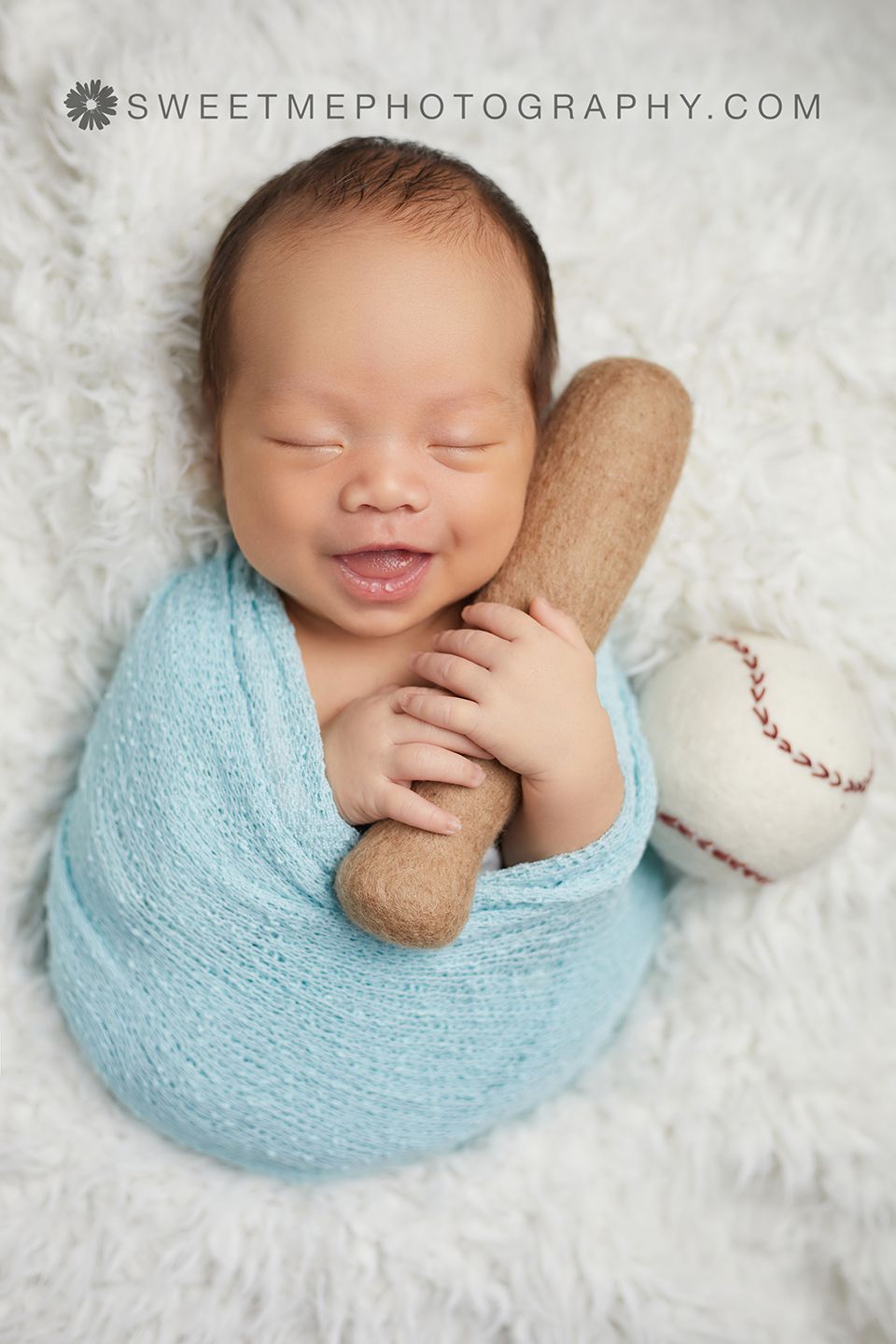 Sleeping newborn wrapped in soft blue swaddle lying on white blanket with baseball props.