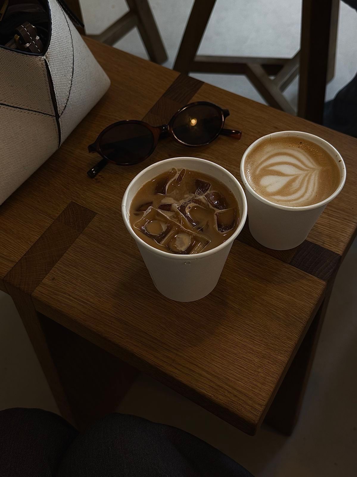 Four ceramic cups with coffee and latte art sit on wooden serving boards in a minimalist cafe setting.