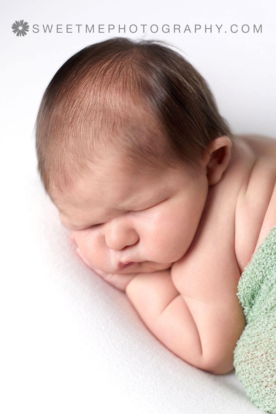 Peaceful sleeping newborn baby wrapped in mint green blanket photographed in soft natural light.