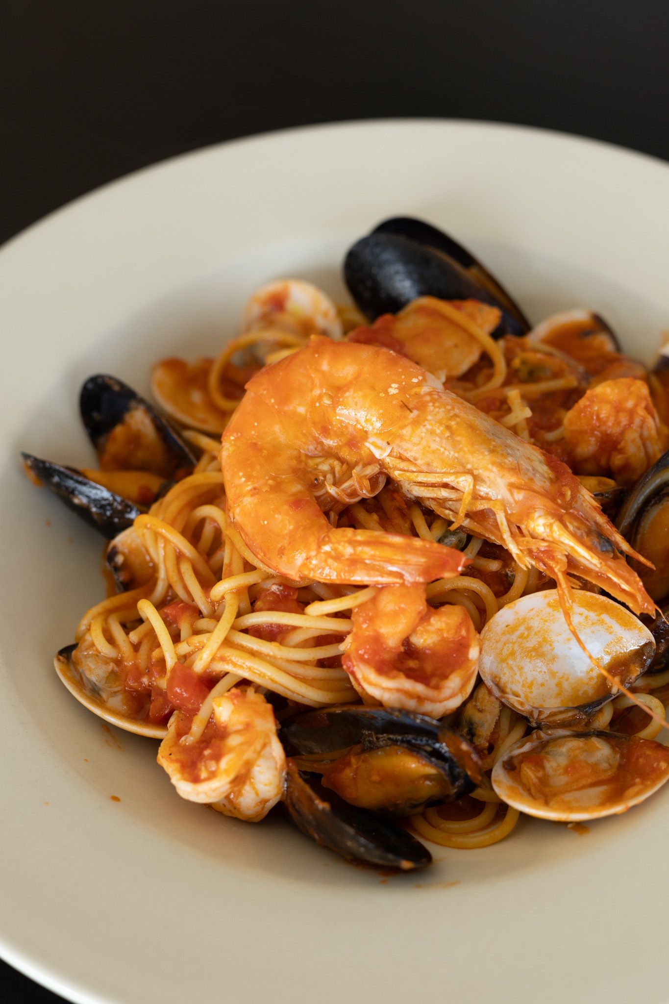 Seafood spaghetti with shrimp, mussels, and clams in tomato sauce served on a white plate.