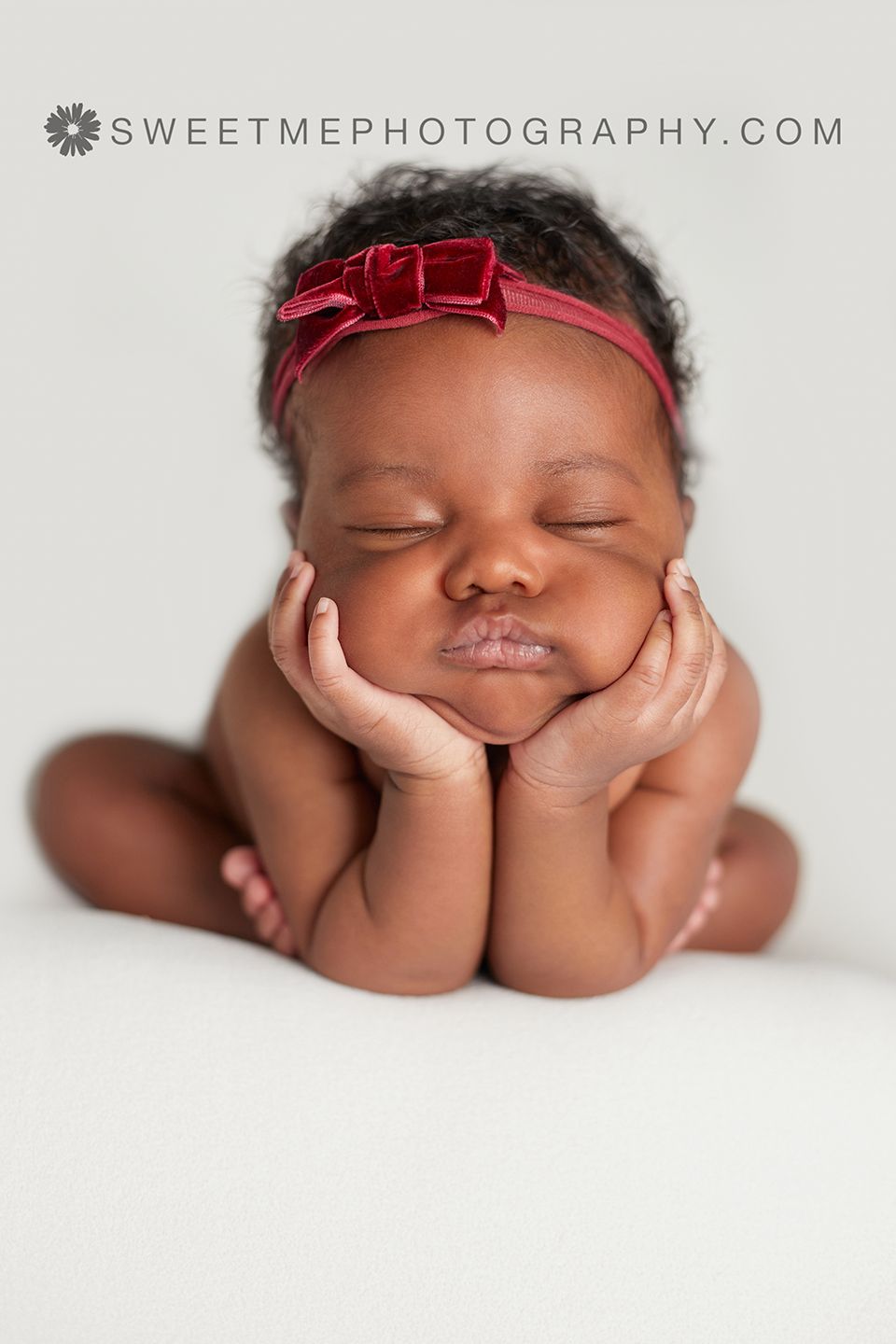 Sleeping newborn with red headband resting peacefully on white backdrop.