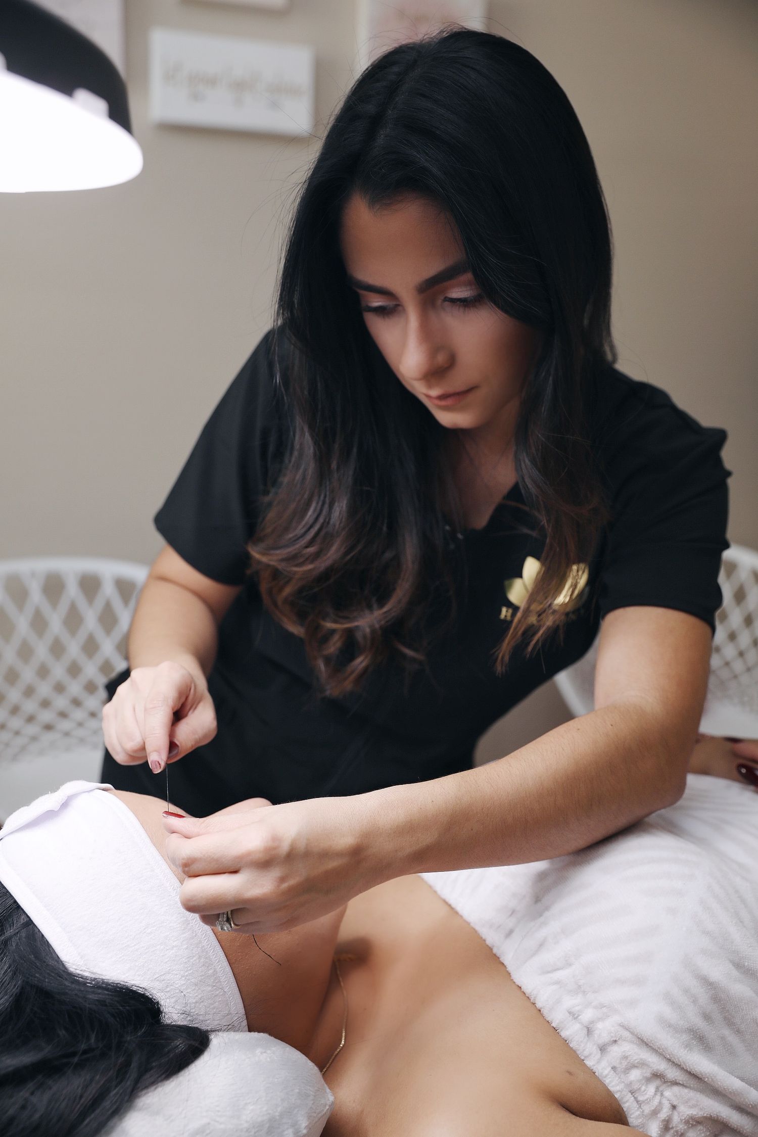 A massage therapist in black attire performs therapeutic massage techniques on a client lying on a white treatment table.