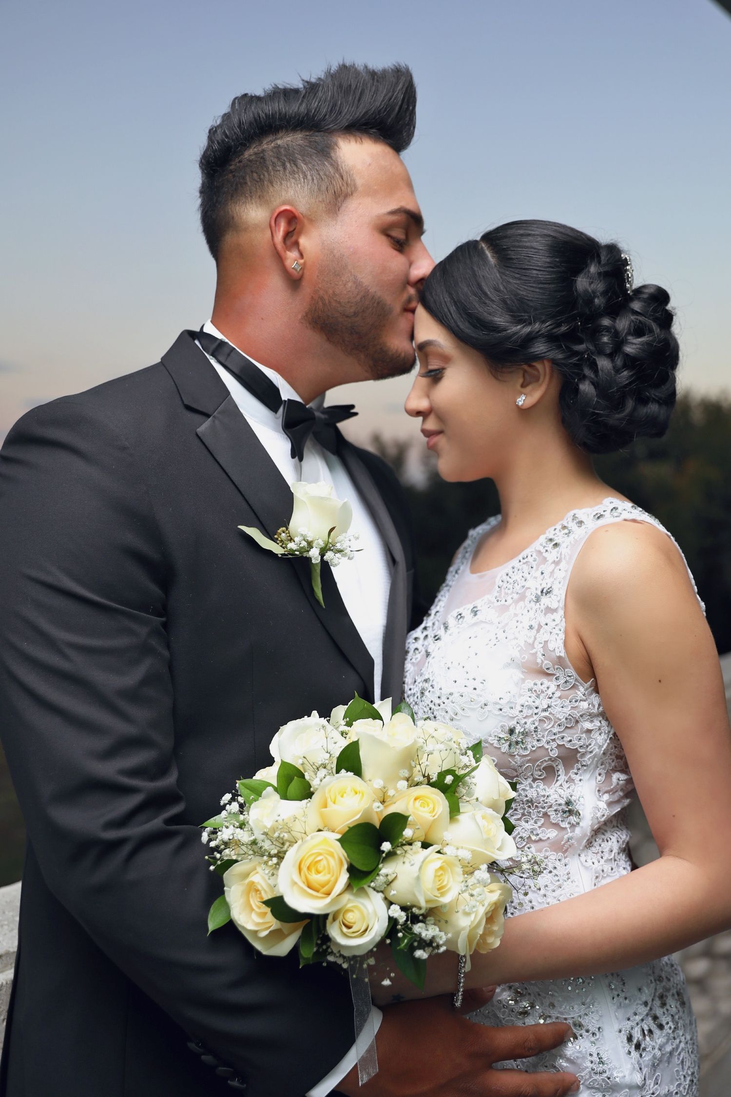 A romantic wedding moment with a couple embracing, featuring a beautiful white rose bouquet and elegant formal attire.
