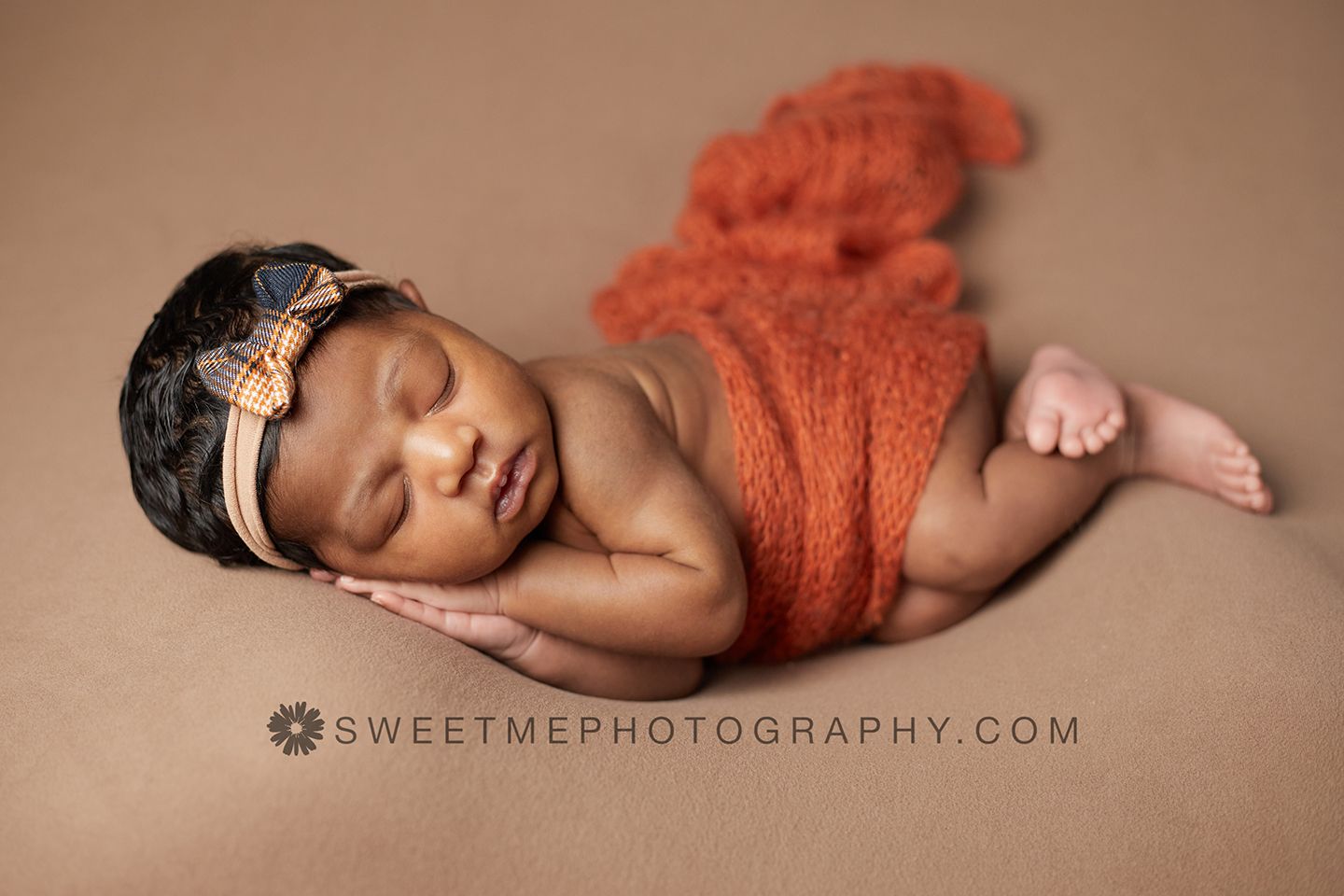 Sleeping newborn baby wrapped in coral knit fabric lying on brown backdrop during professional photo session.