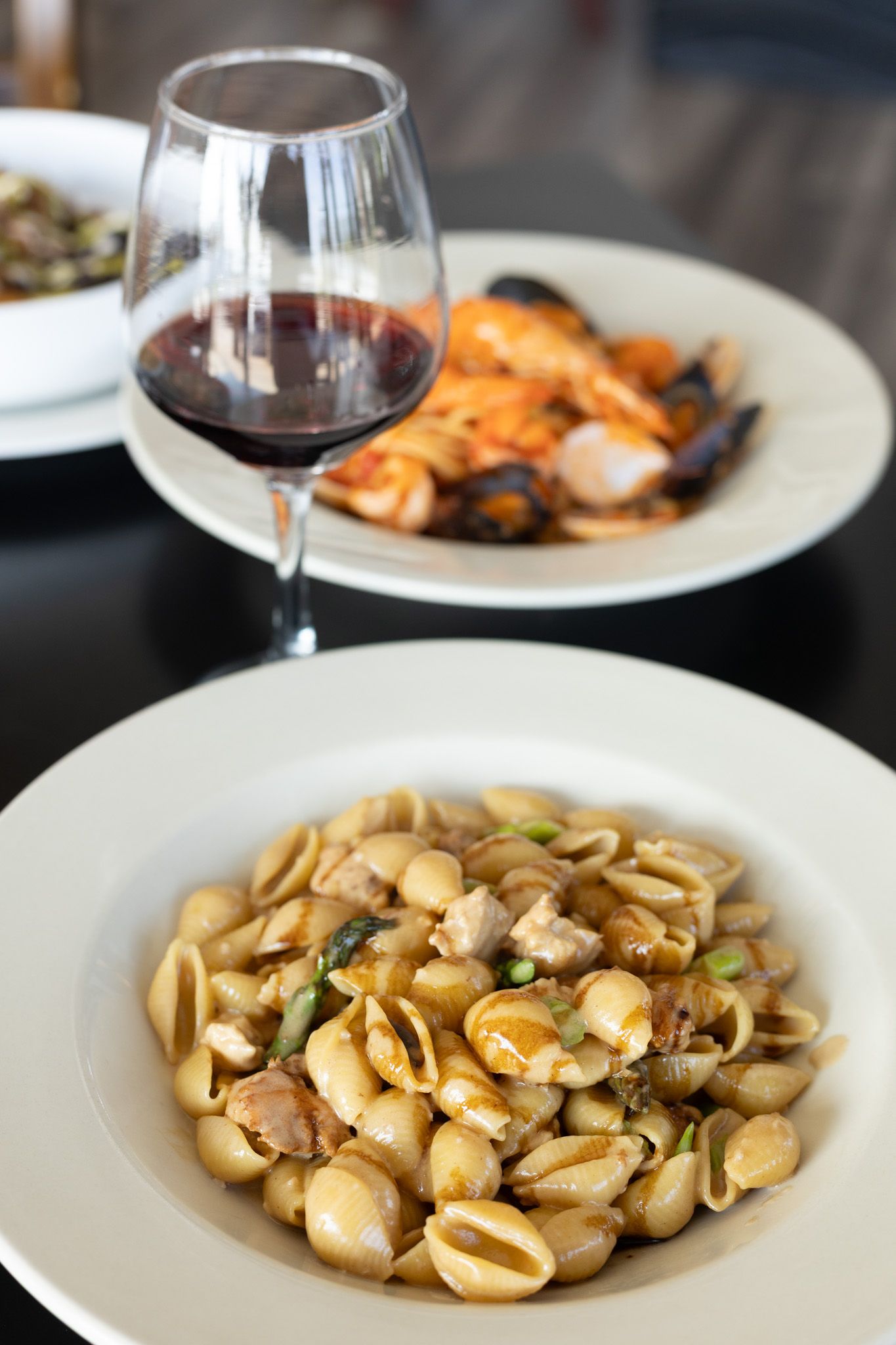 Shell pasta with seafood and herbs in a creamy sauce served on white plates with red wine glasses.