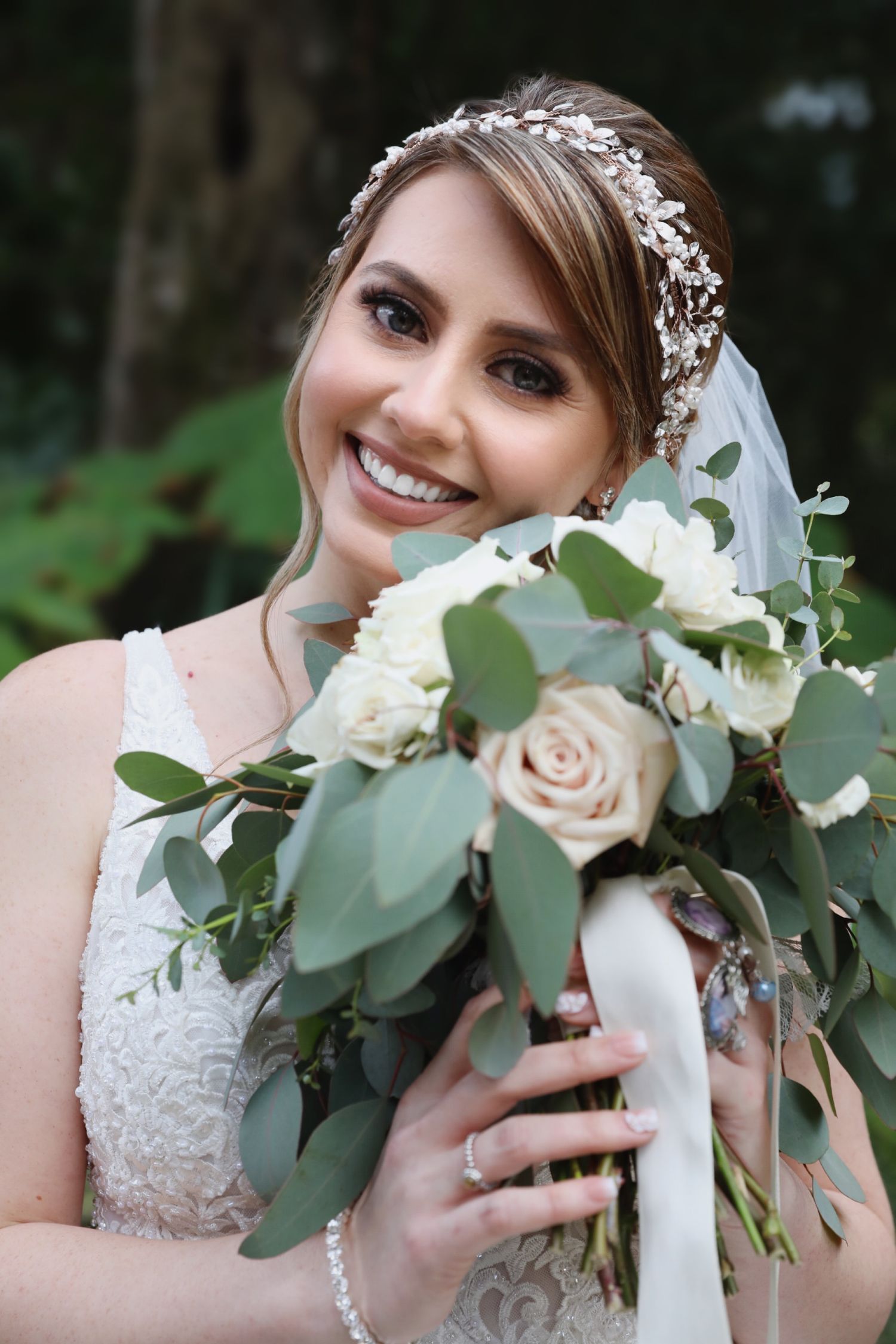 Beautiful bridal portrait with white roses and eucalyptus bouquet against natural outdoor background.