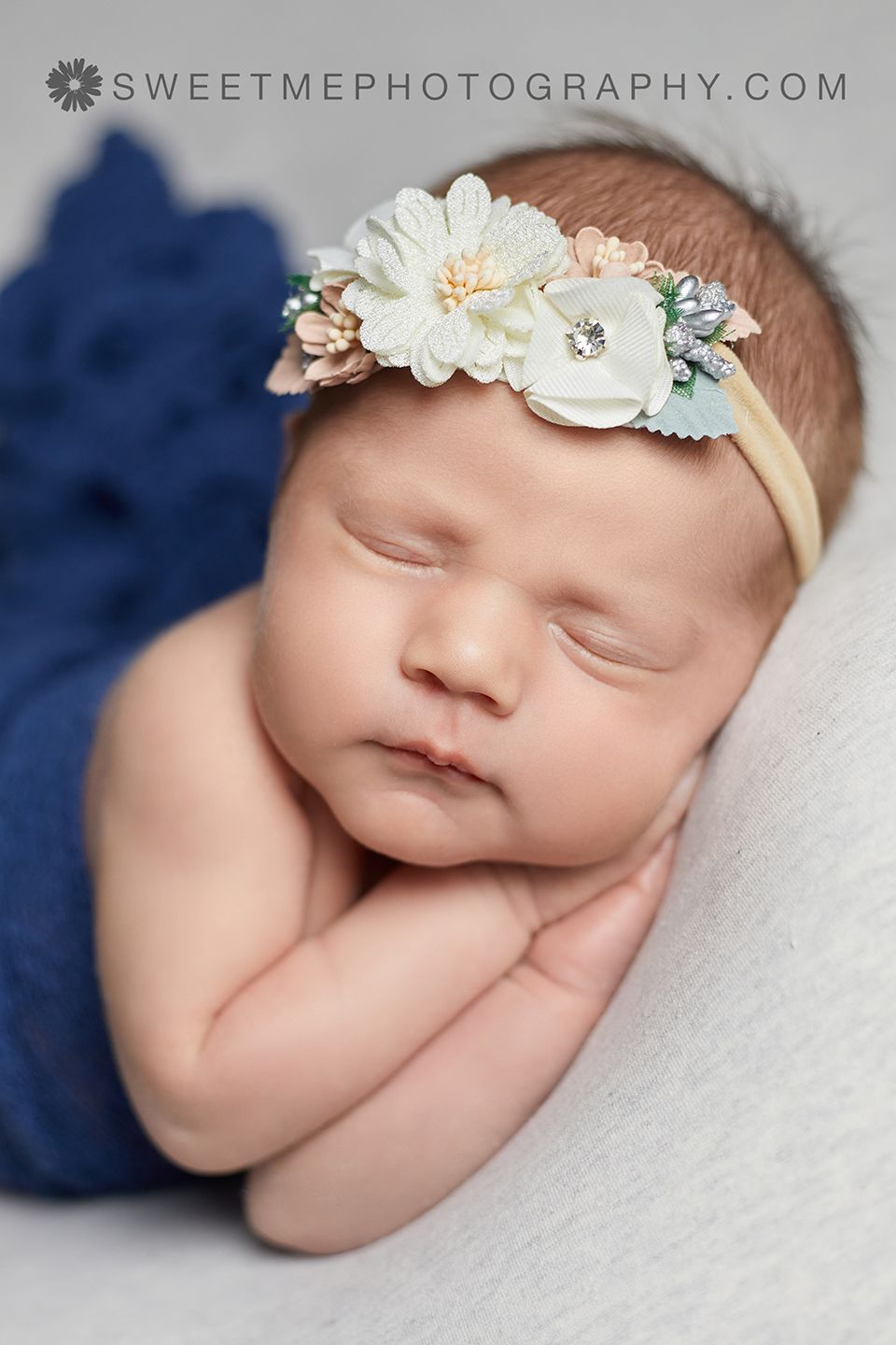 Sleeping newborn with delicate floral headband against blue and white background.