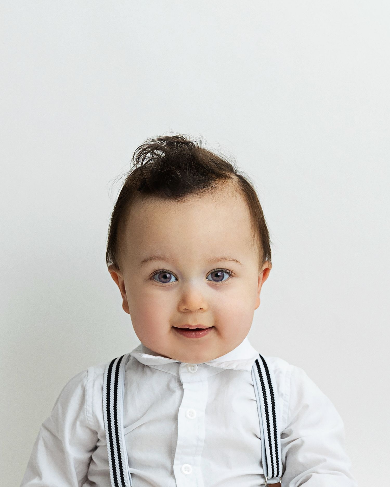 A baby in a white sailor-style outfit smiles while sitting against a light background.