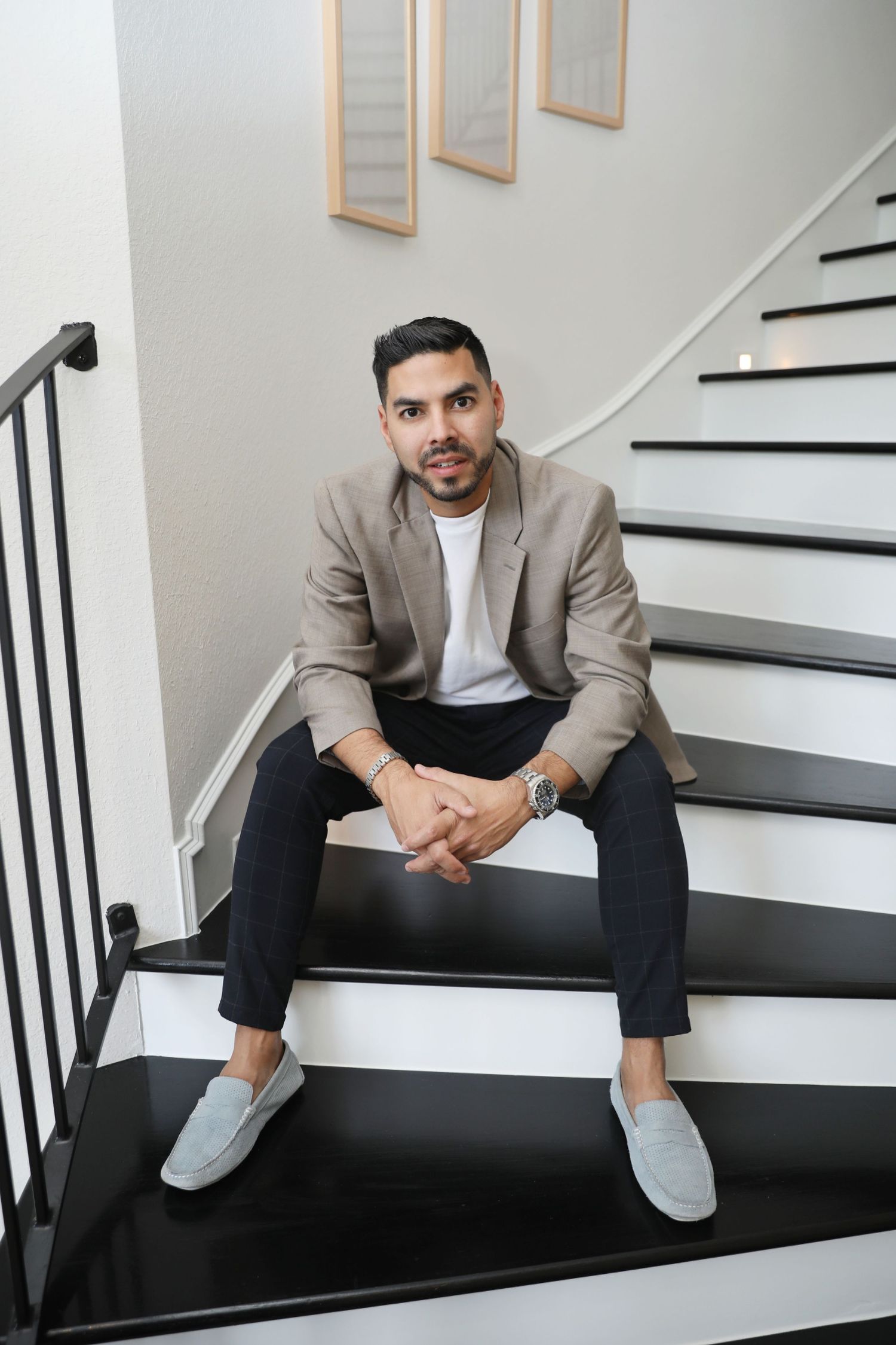 A person in a beige blazer and gray loafers sits on black and white stairs in a modern home interior.
