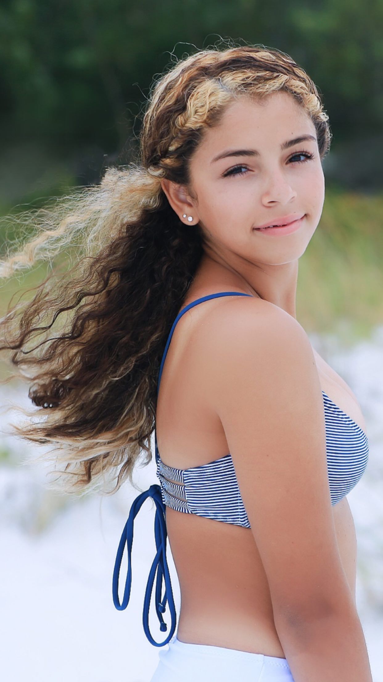 A series of four photos showing a person with long curly hair in a blue and white striped swimsuit posing outdoors.