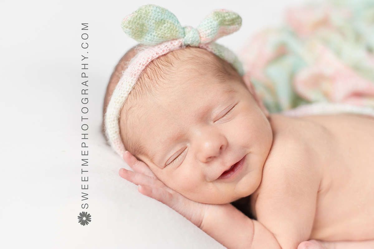 Peaceful sleeping newborn baby with mint green bow headband resting on soft blanket during professional photo session.