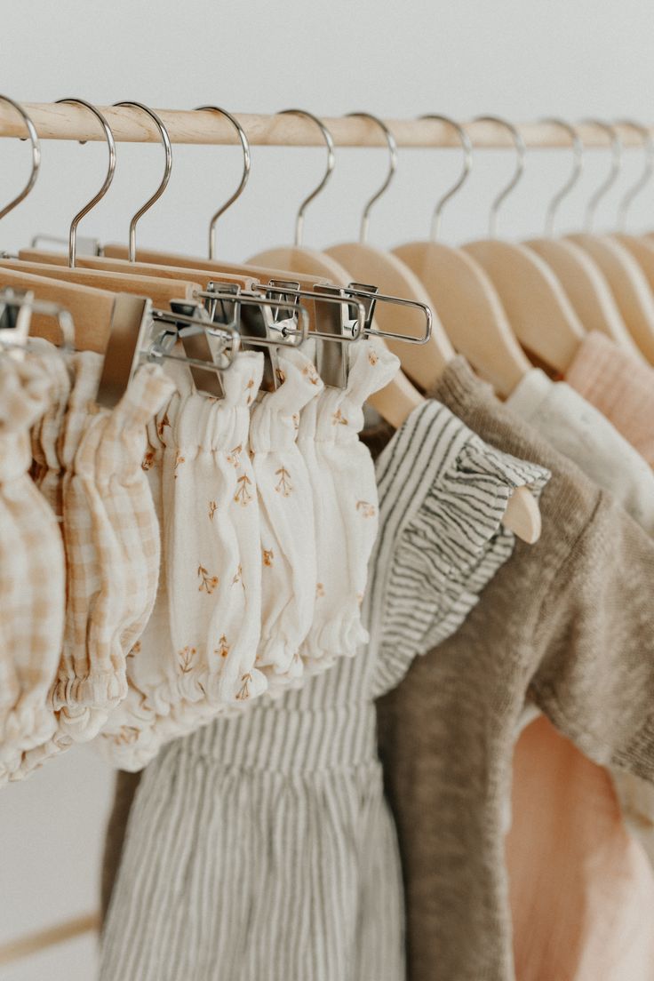 Neutral-toned baby clothes hanging on wooden hangers on a clothing rack, featuring soft pastels and delicate patterns.