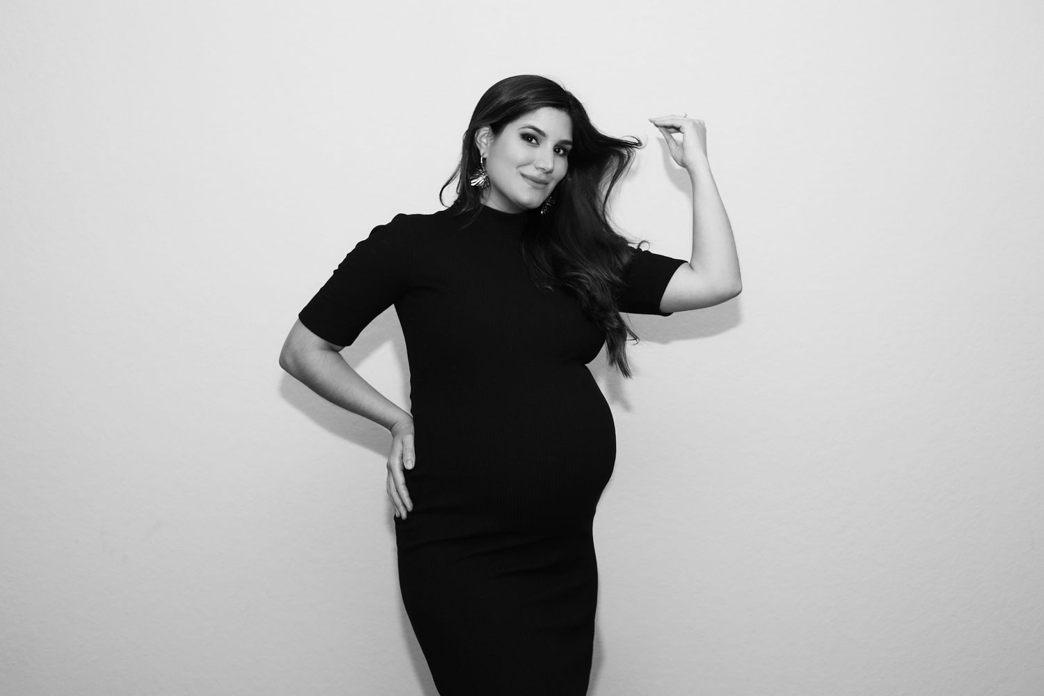 Black and white portrait of a pregnant woman in a dark turtleneck dress posing against a light background.