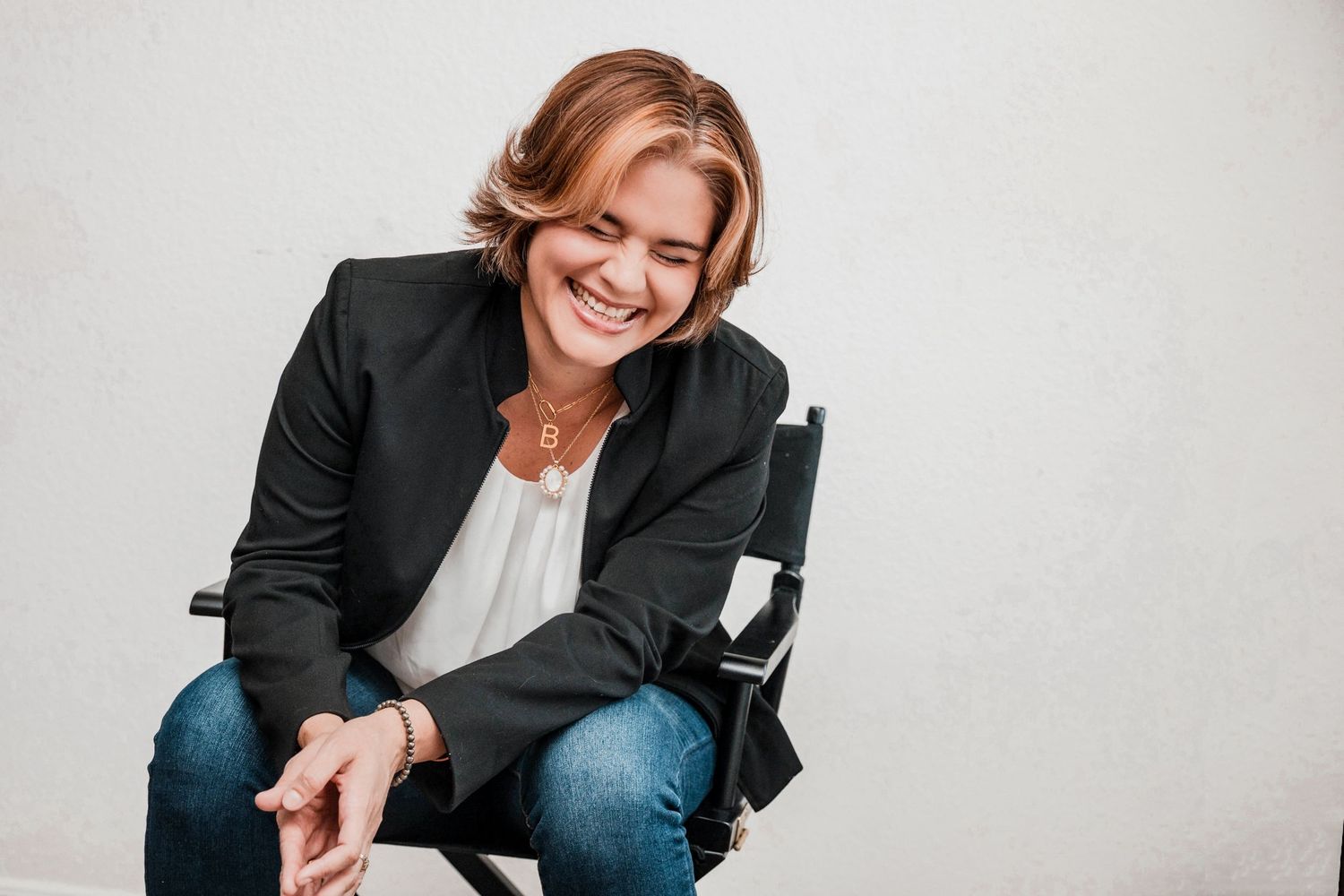 Professional in business attire smiles warmly while sitting in casual poses during a photo session.