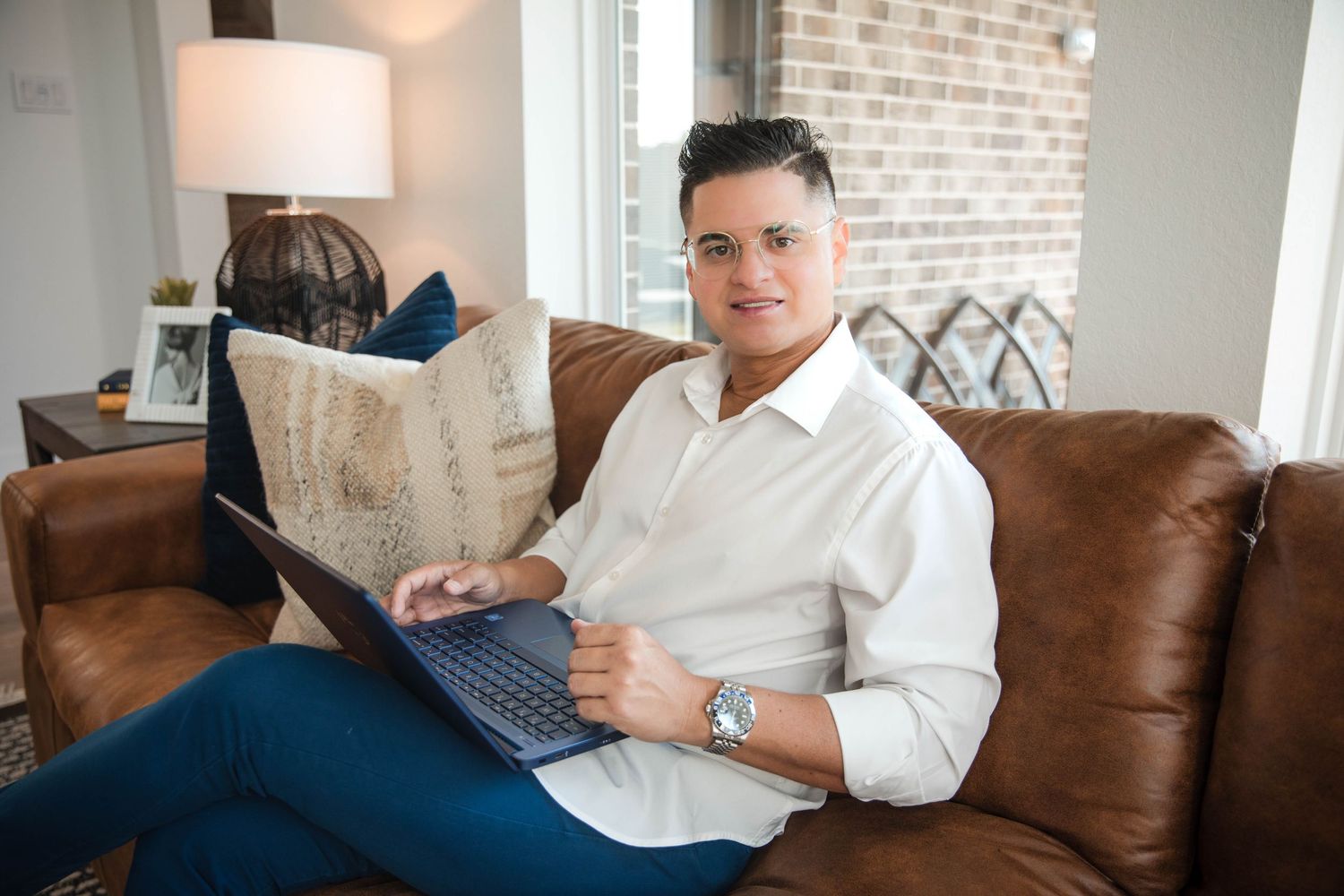 Person relaxing on brown leather couch while reading on digital tablet in modern living room with brick wall.
