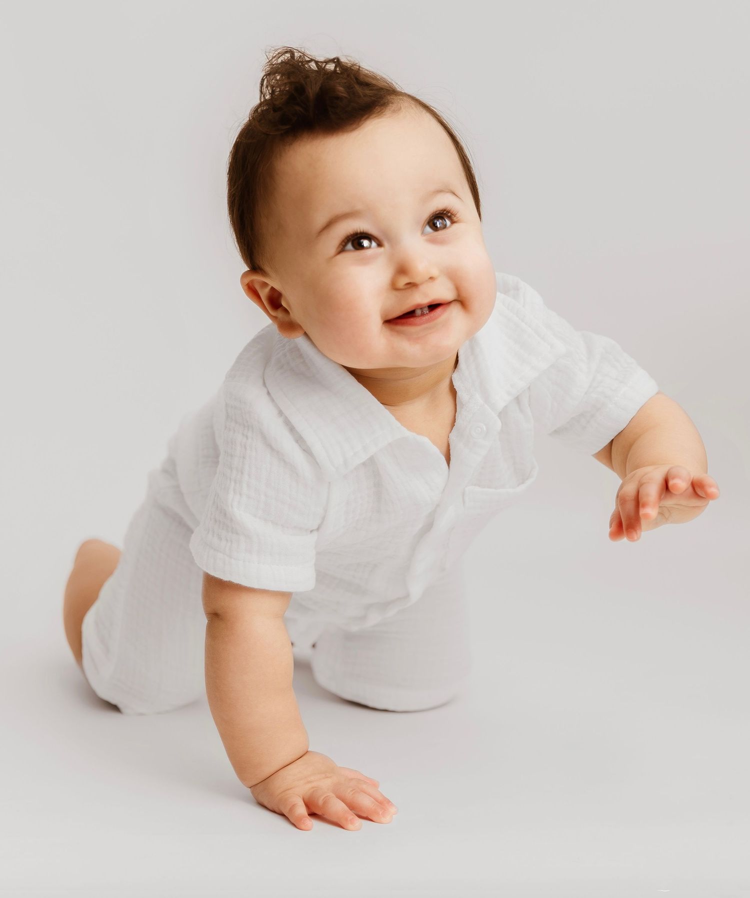 Baby in white outfit crawls and smiles on white background in series of playful poses.