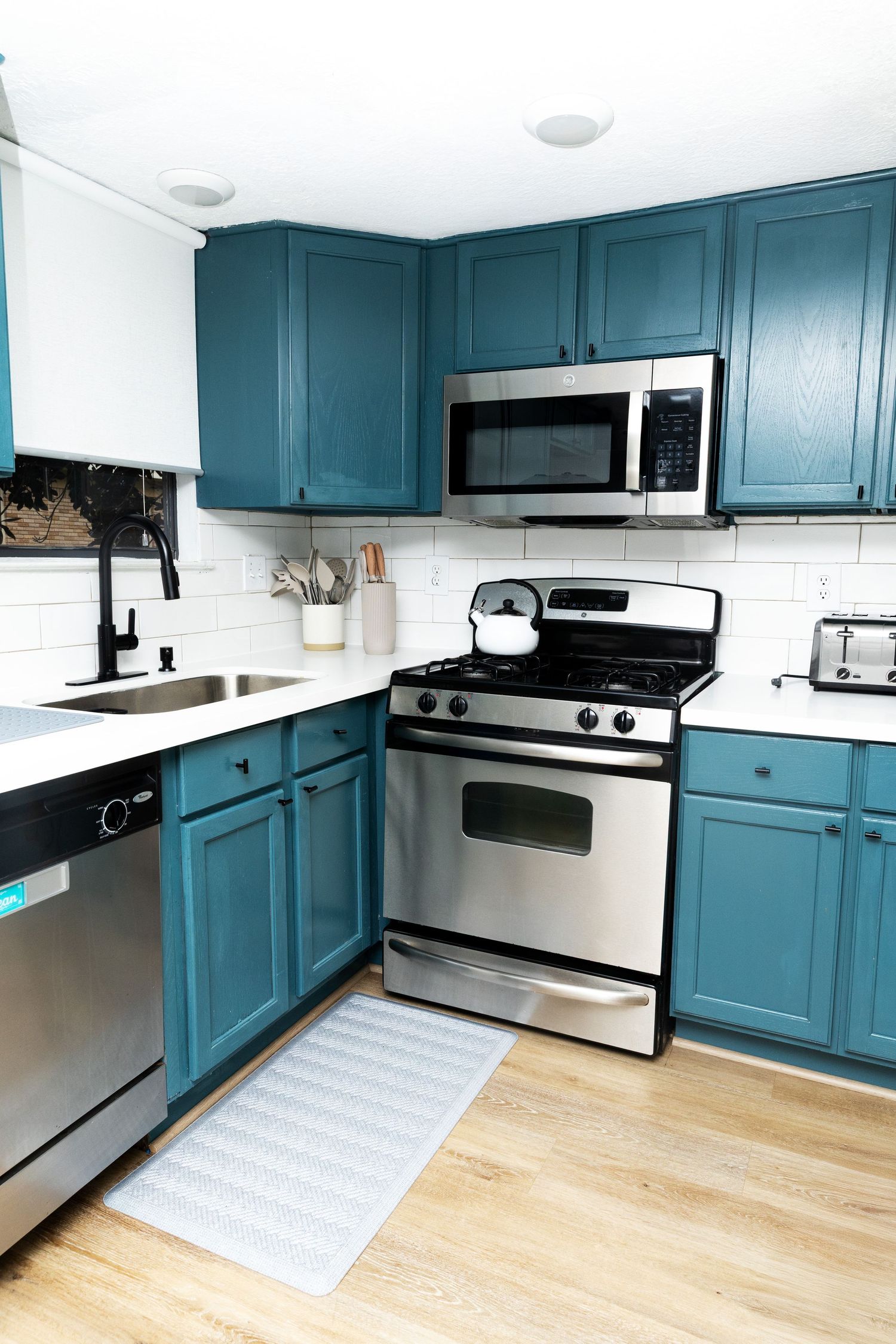 Teal kitchen cabinets with stainless steel appliances, white subway tile backsplash, and hardwood floors.