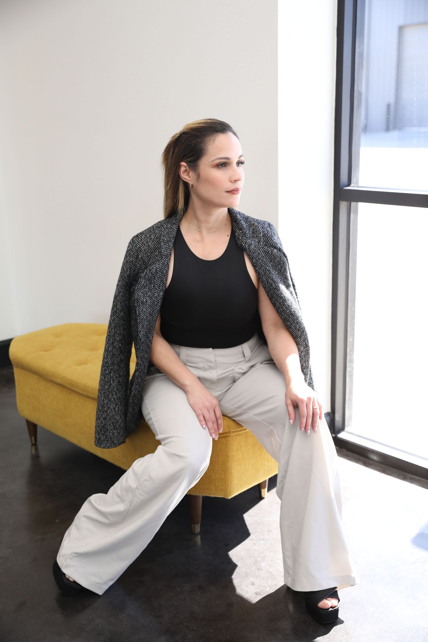 A series of fashion poses on a yellow couch showing flowing white pants and a black top with gray sweater.