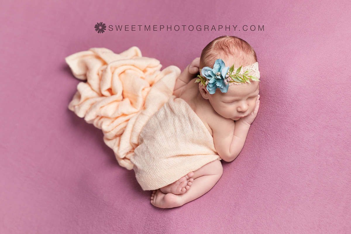 Sleeping newborn in peach wrap on pink background with soft studio lighting.