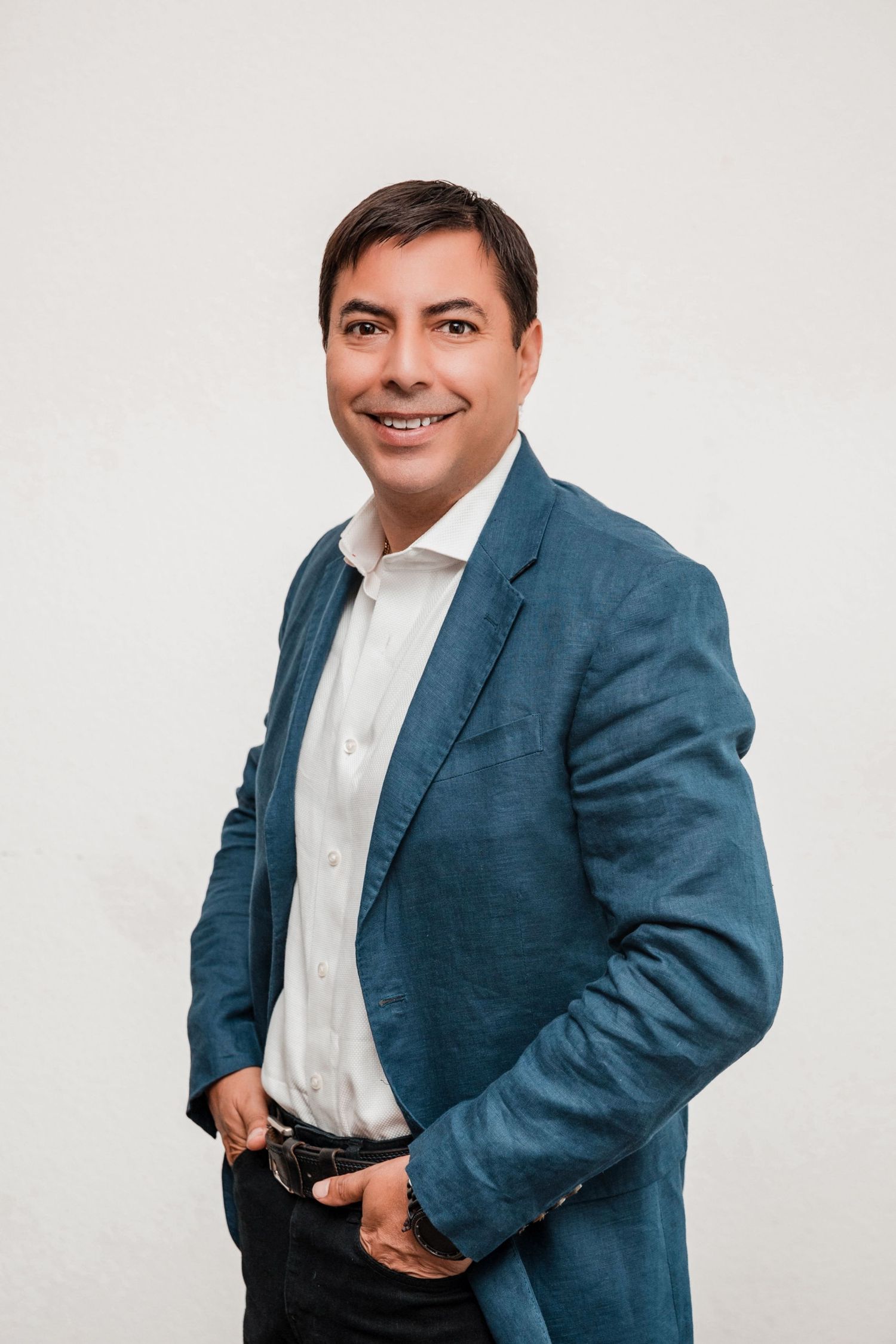 Professional portrait of someone wearing a teal blazer and white dress shirt against a light background.