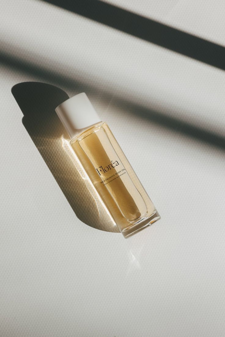 Florea glass perfume bottle with golden liquid and white cap on white textured surface with dramatic shadows.
