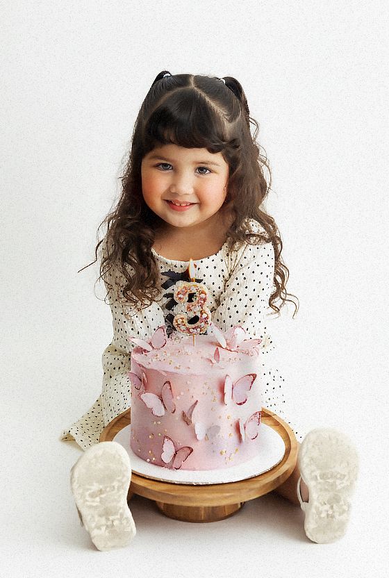 Pink butterfly cake sits on wooden stand with child in polka dot dress.