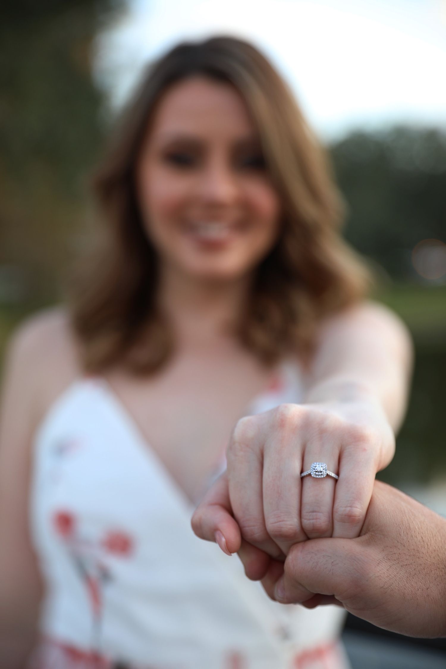 Close-up photo showing a newly engaged couple holding hands and displaying an engagement ring outdoors.
