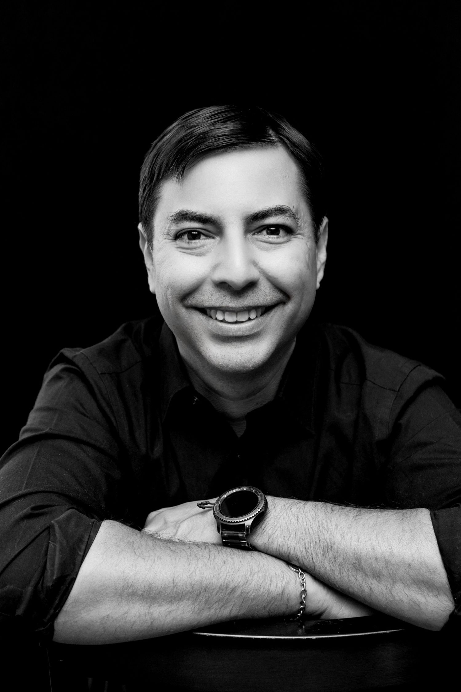 Black and white portrait sequence showing a person resting on their arms with a bright smile against dark background.