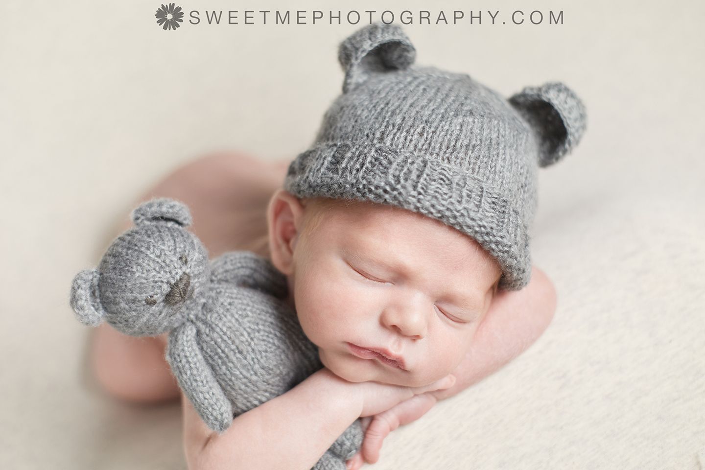 Sleeping newborn wearing knitted gray bear hat and matching teddy bear during portrait session.