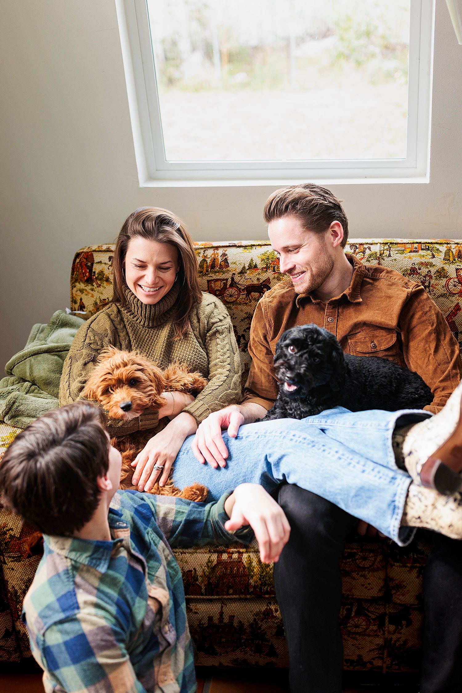 parents snuggle dogs on couch while son talks to them by Austin family photographer