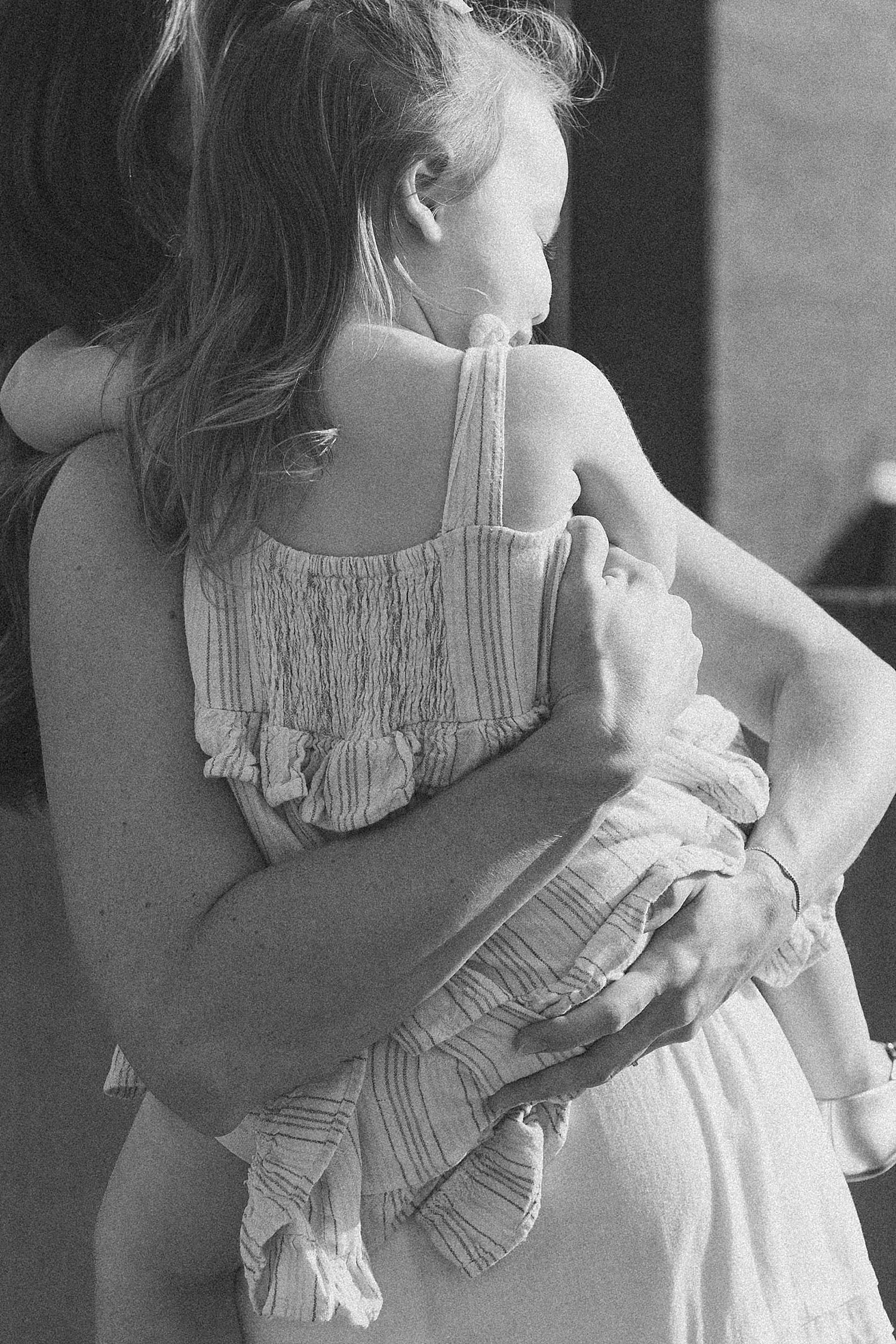 mother holds her daughter in dress close by Claire Malaby Photo
