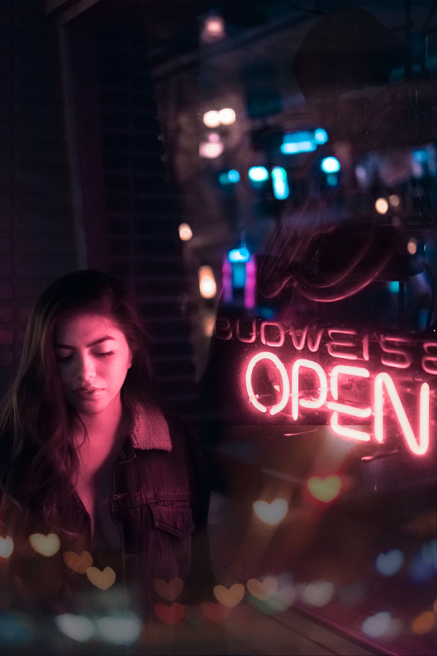 Artistic night portrait with pink neon OPEN sign, heart-shaped bokeh lights, and soft urban glow creating a dreamy cinematic atmosphere.