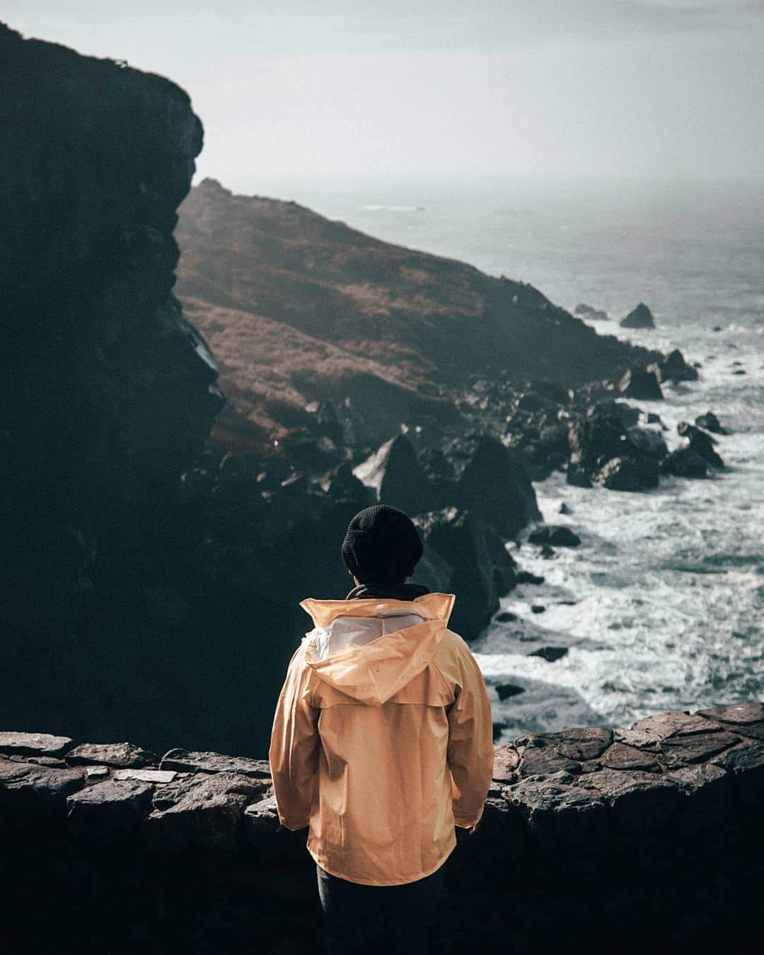 Person overlooking a coastal cliff at sunset with waves crashing below, capturing a calm and scenic shoreline adventure.