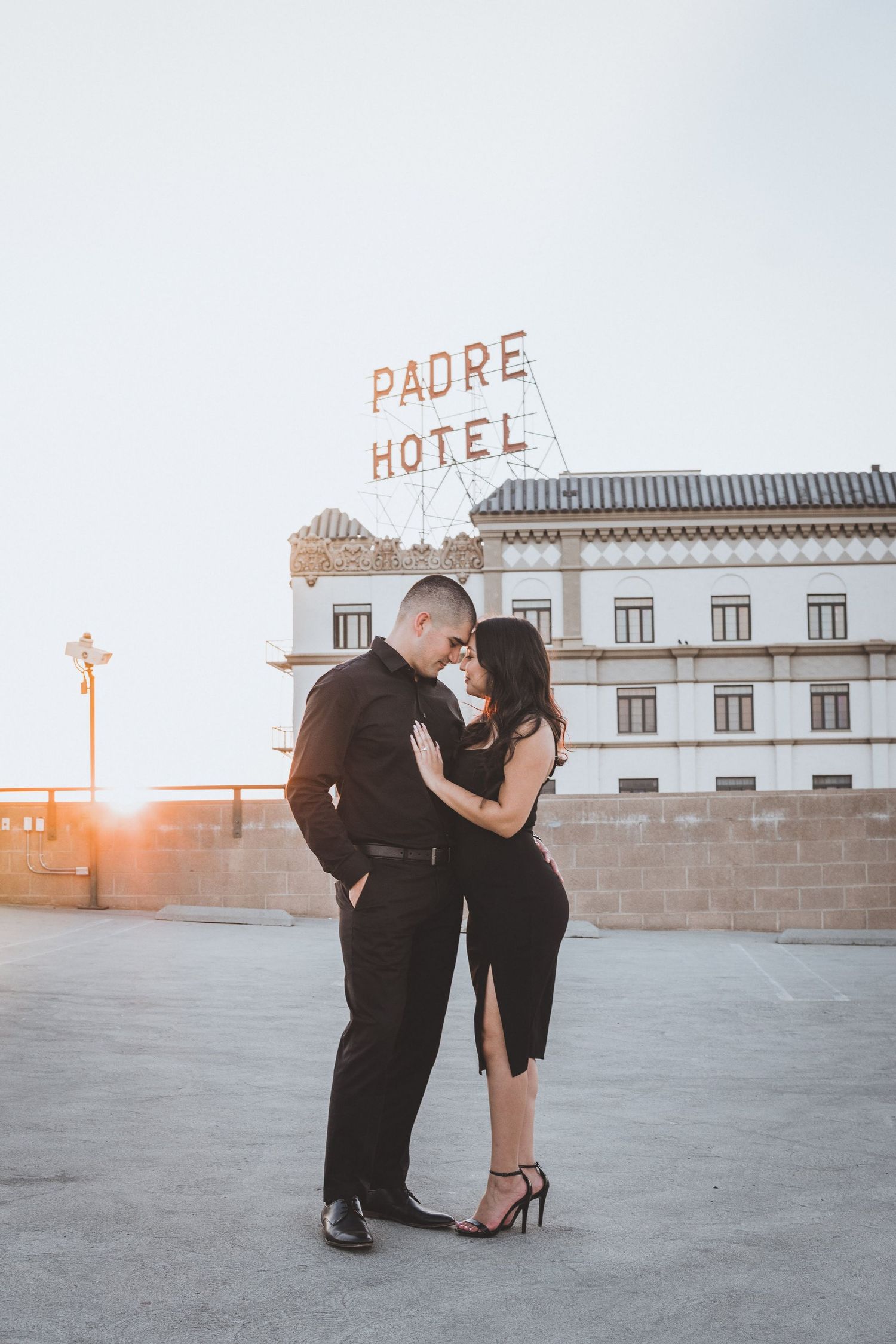 Elegant couple embracing on a rooftop at sunset with a historic hotel sign in the background, creating a romantic urban portrait scene.