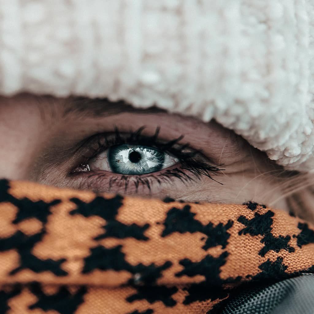 Close-up minimal portrait showing striking blue eyes framed by winter clothing, highlighting detail, emotion, and outdoor atmosphere