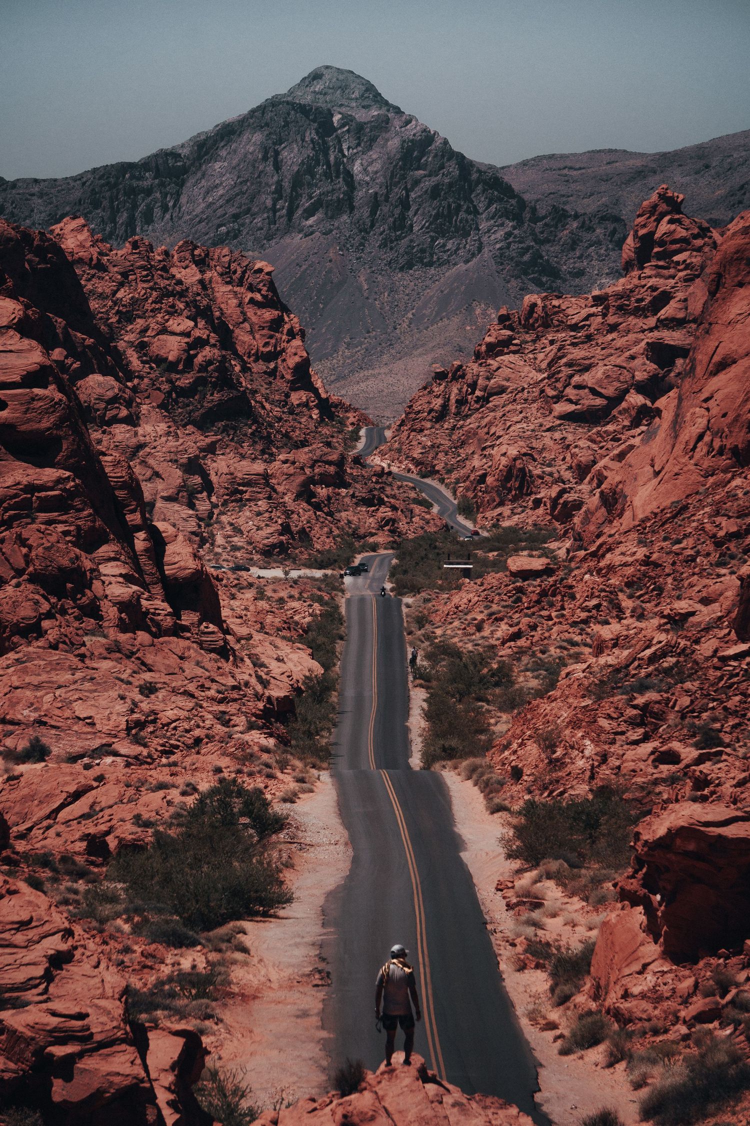 Man exploring a rocky desert landscape with red canyon walls in the background during a warm outdoor adventure.