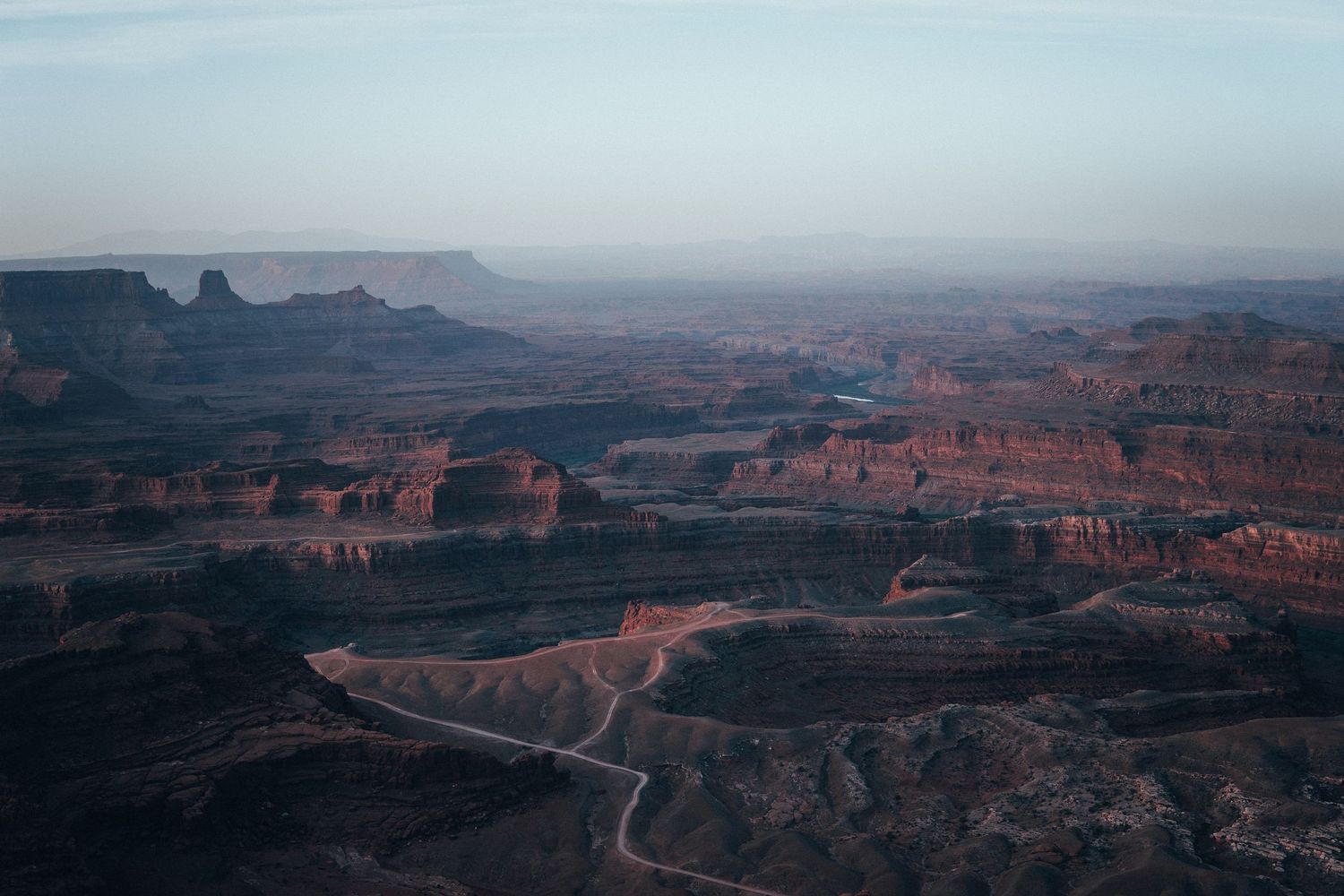 Aerial canyon landscape with layered red cliffs, winding river, and soft morning haze highlighting the depth of a vast desert adventure terr
