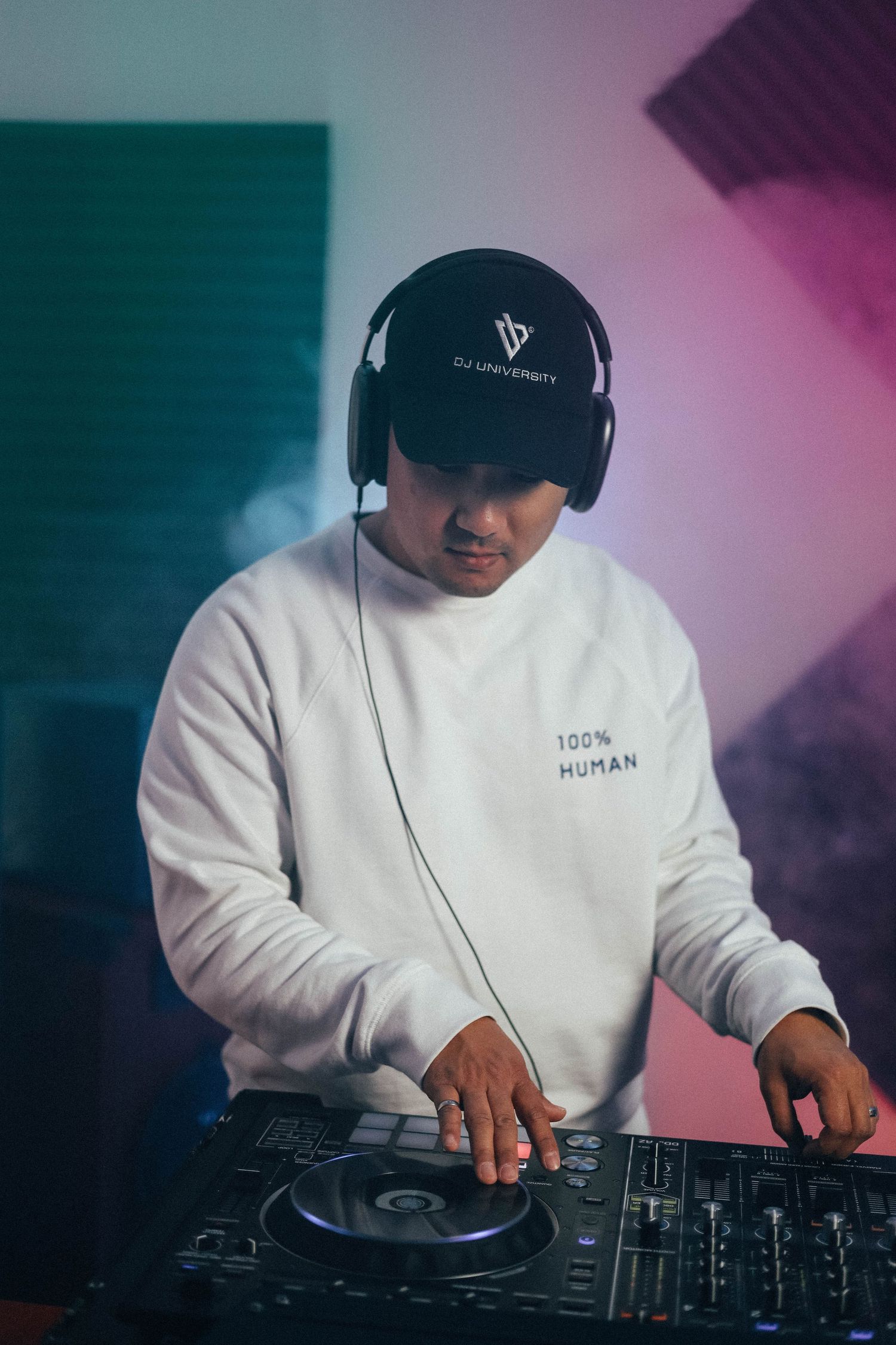 DJ mixing music indoors with headphones and colored studio lighting, focused on turntables and electronic equipment in a creative workspace.