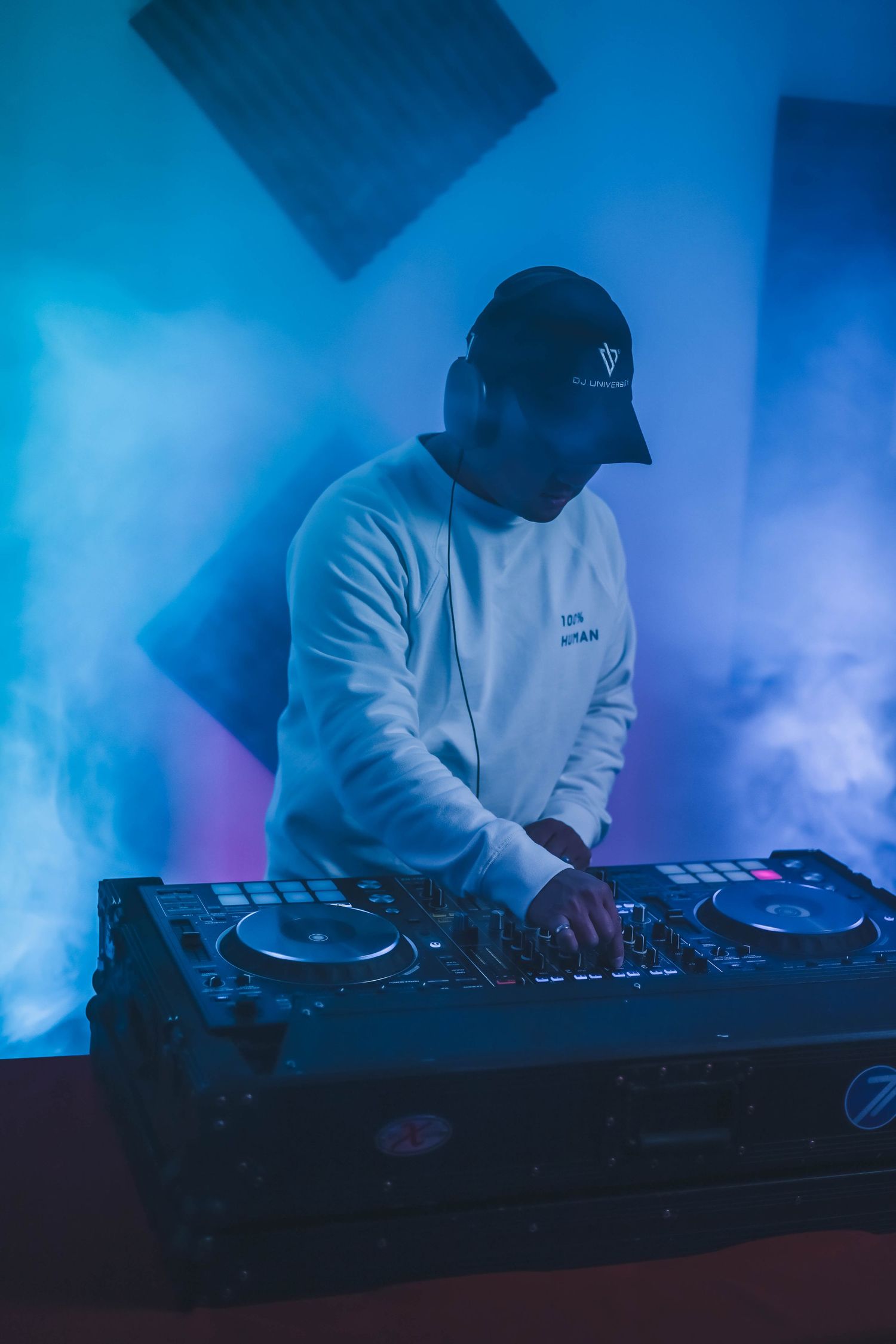 DJ mixing music indoors with headphones and colored studio lighting, focused on turntables and electronic equipment in a creative workspace.