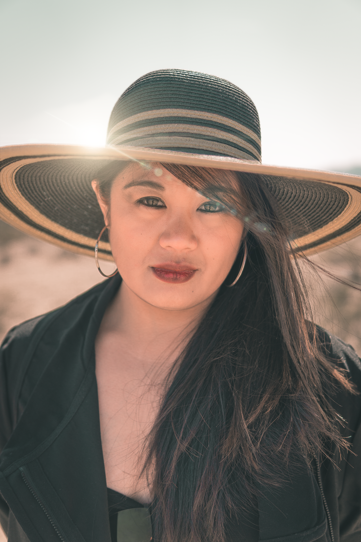 Stylish portrait of a woman wearing a wide-brim hat in desert sunlight, warm tones and soft lens flare creating a modern fashion look