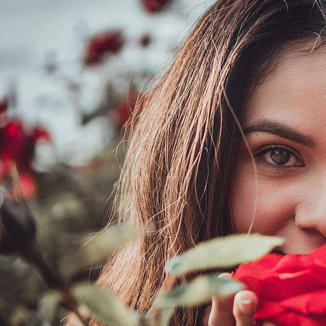 Close-up portrait of a woman holding vibrant red roses in a garden, soft focus florals and dreamy natural light highlighting her eyes