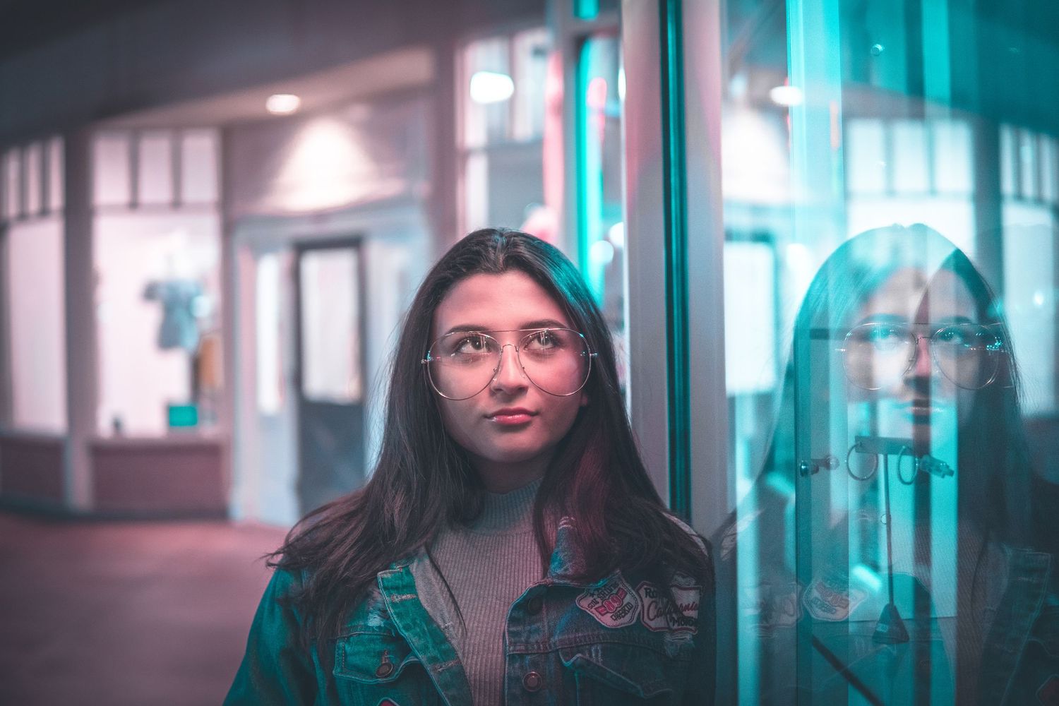 Woman standing before an illuminated mirror in low warm light, creating a cozy indoor moment with soft aesthetic tones